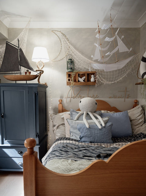 3. Nautical-themed child's room with 'Adventure Awaits' wooden sign above bed, ship model, and octopus plush