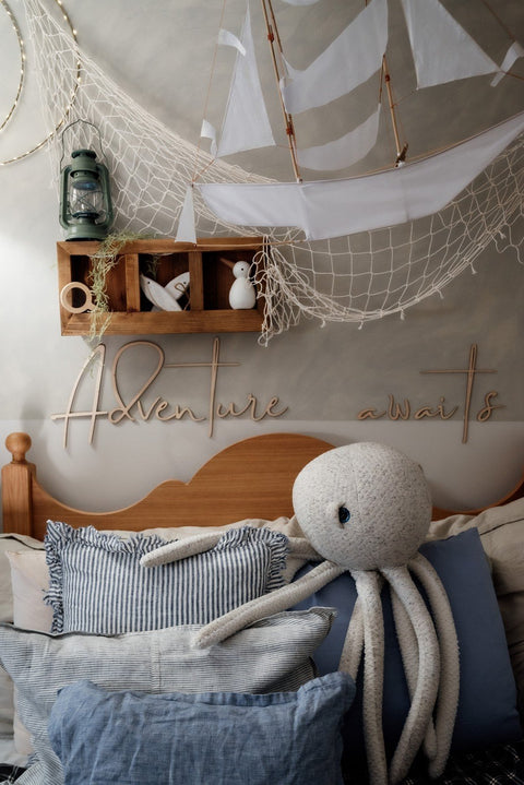 1. Child's room with nautical theme featuring wooden wall sign 'Adventure Awaits' above bed with octopus plush and decorative netting