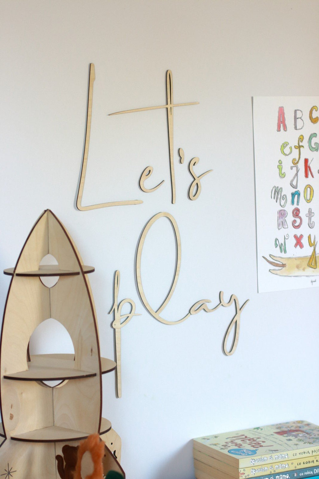 2. Natural plywood 'Let's Play' wall sign in children's room with wooden rocket shelf and colorful alphabet poster