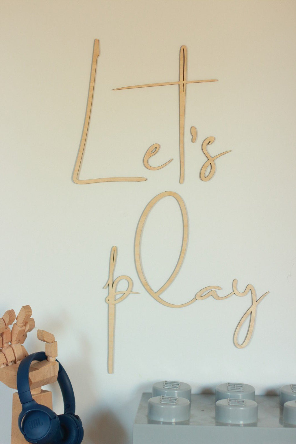 3. Natural plywood 'Let's Play' wall sign in children's play area with wooden toys and headphones on a shelf