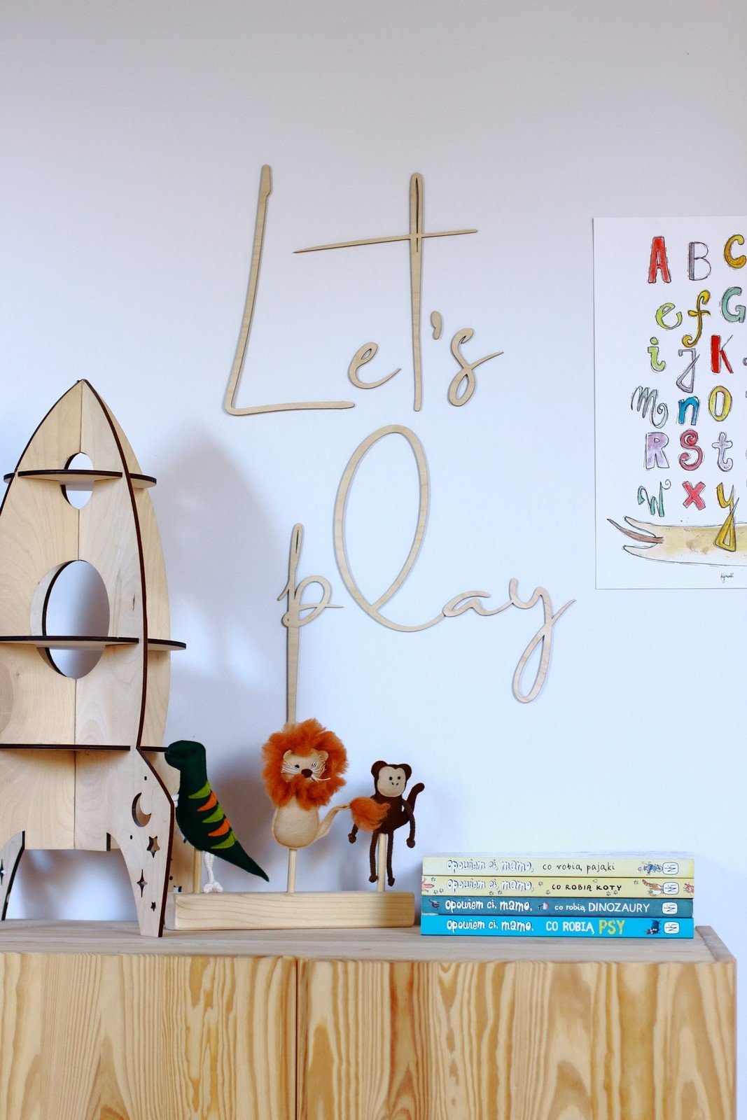 1. Children's room with natural plywood 'Let's Play' wall sign above wooden toys and books on a shelf