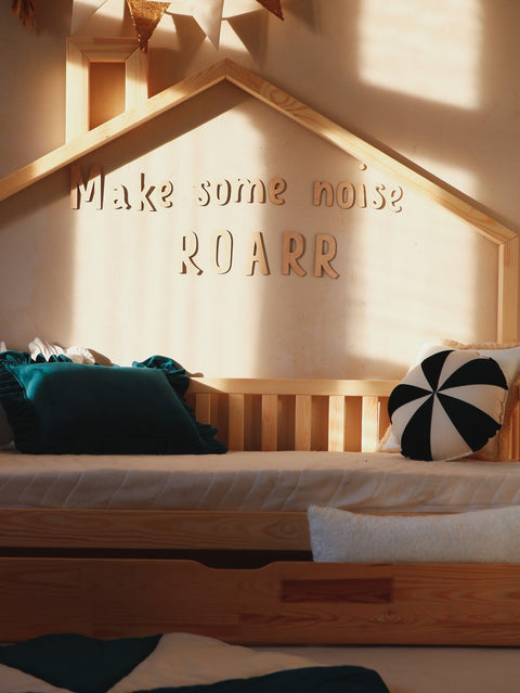 4. Wooden wall sign 'Make some noise ROARR' above bed with green and black pillows in child's room