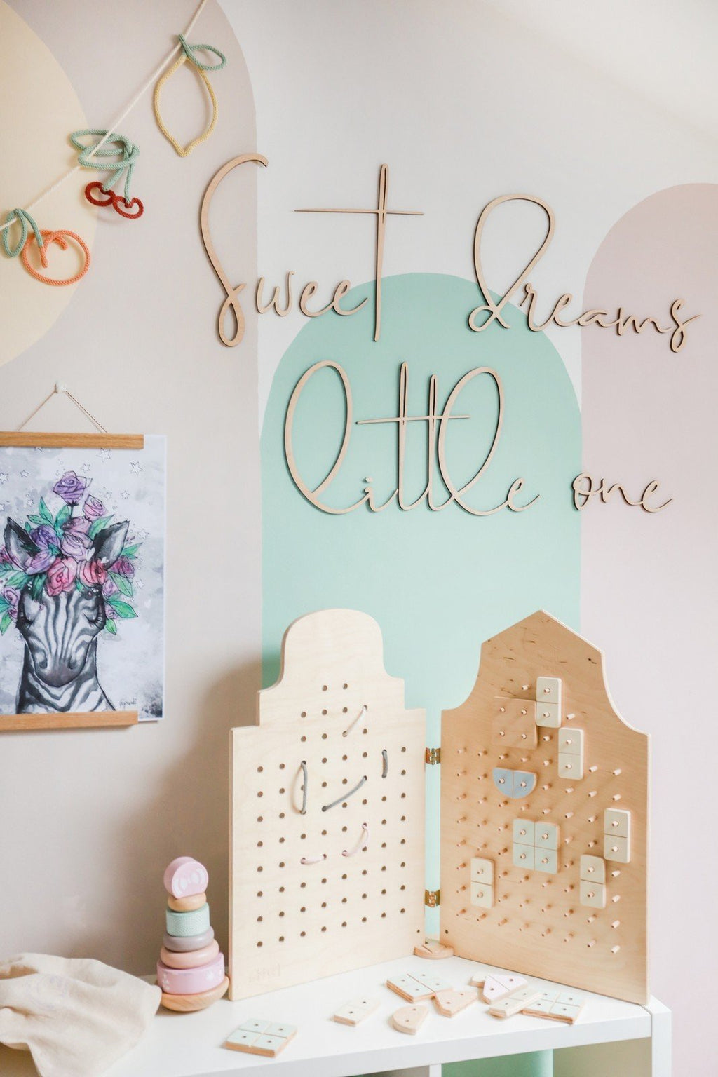 7. Playroom with wooden 'Sweet Dreams Little One' sign on pastel wall above activity boards and toys