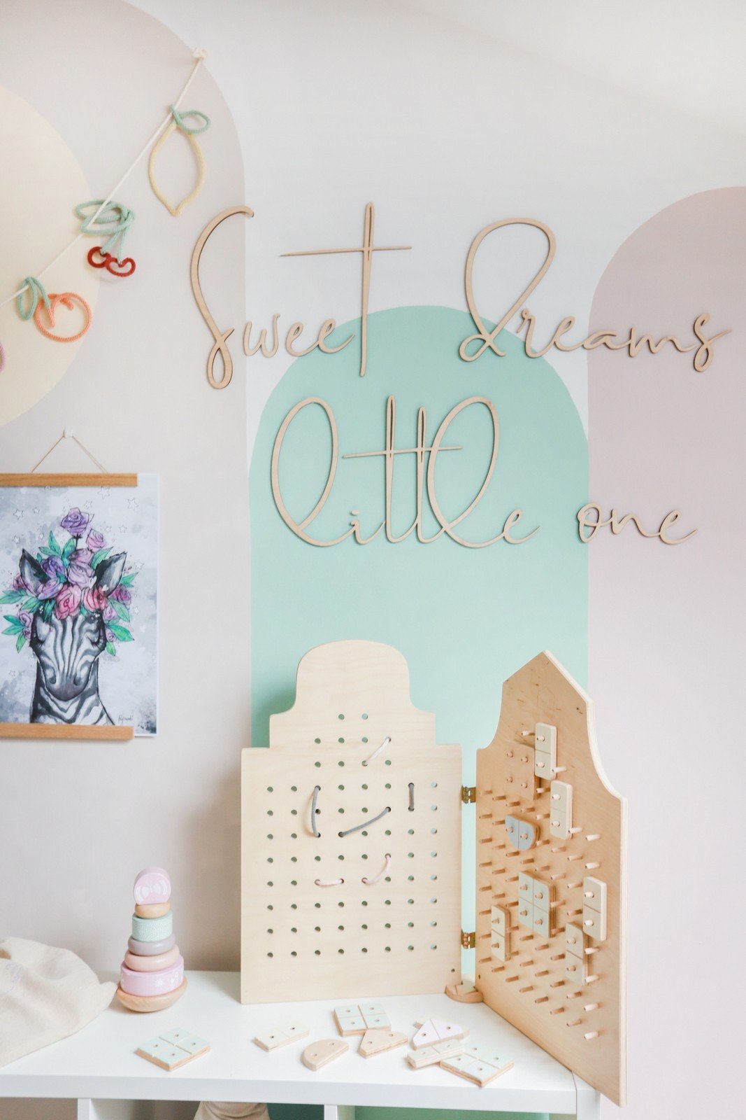 4. Playroom with wooden 'Sweet Dreams Little One' sign on pastel wall above activity boards and toys
