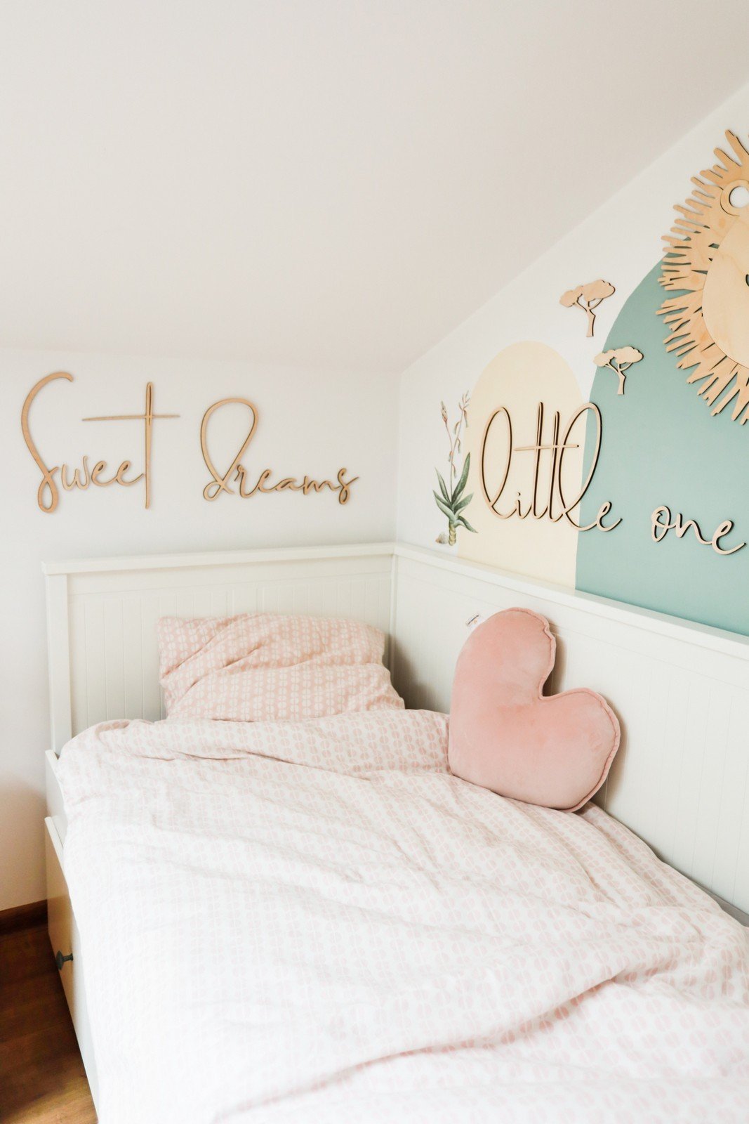 8. Bedroom with wooden 'Sweet Dreams Little One' sign above bed with pink heart pillow and pastel wall art