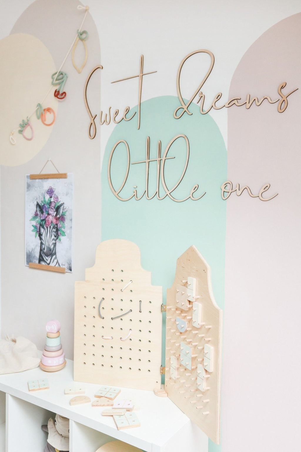 6. Playroom with wooden 'Sweet Dreams Little One' sign on pastel wall above activity boards and toys
