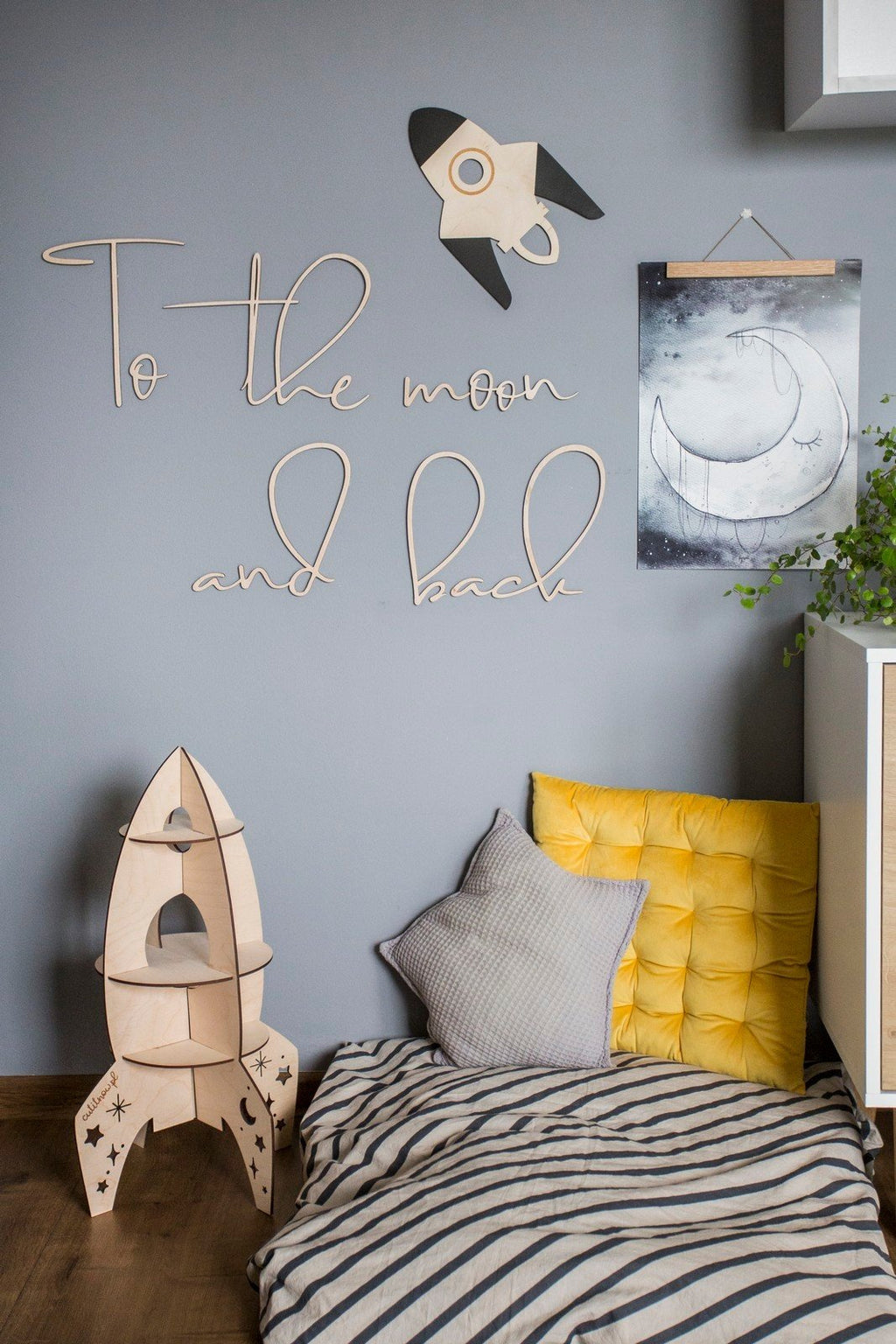 3. Cozy child's room featuring wooden 'To the moon and back' wall sign, rocket decor, and striped bedding, enhancing a playful atmosphere.