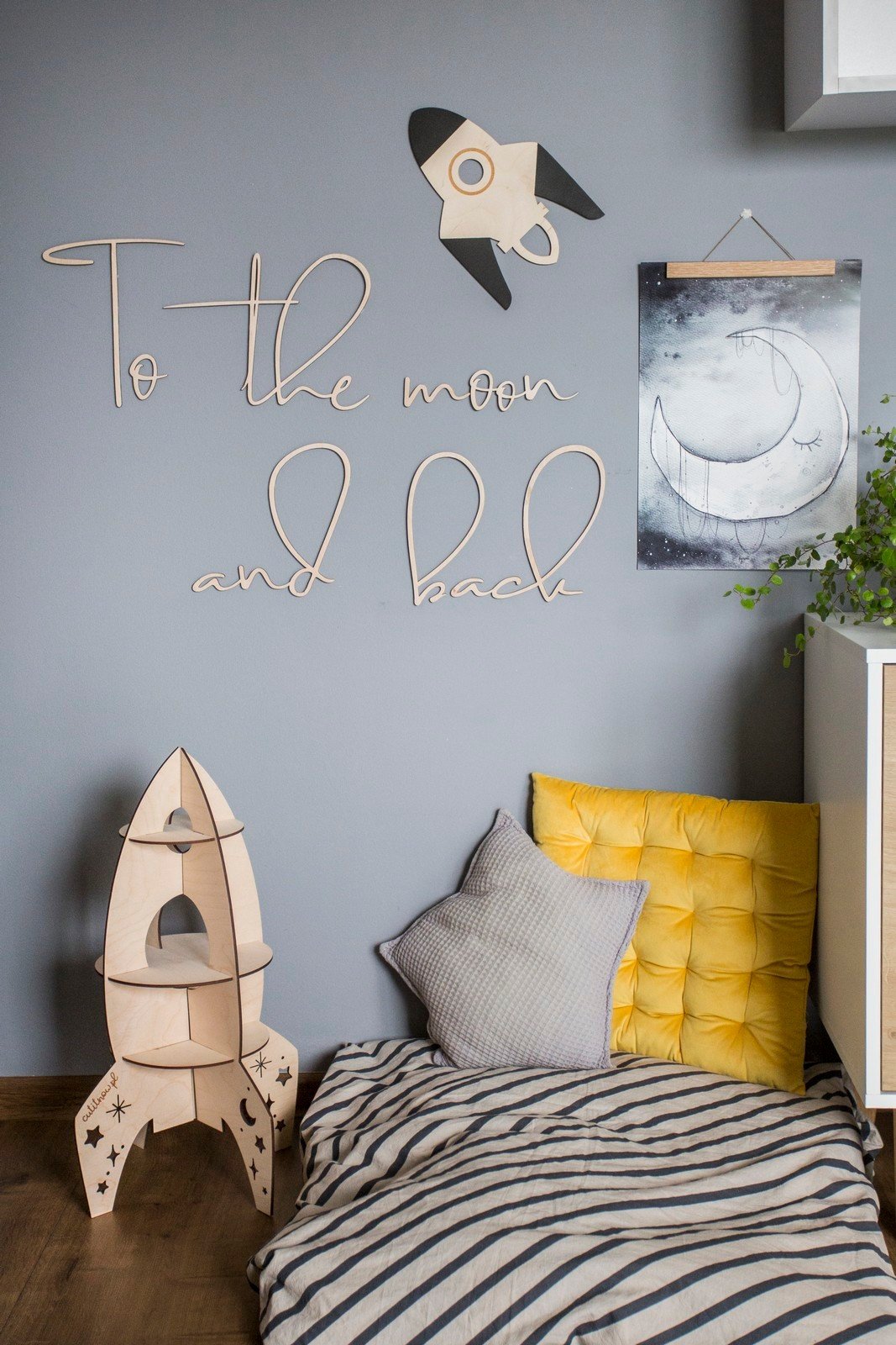 3. Cozy child's room featuring wooden 'To the moon and back' wall sign, rocket decor, and striped bedding, enhancing a playful atmosphere.