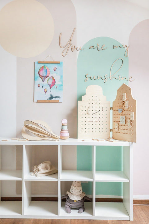 2. Child's room with 'You Are My Sunshine' wooden wall sign, pastel wall art, and wooden toys on a white shelf.