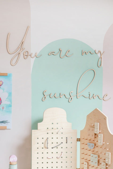 1. Wooden wall sign with 'You Are My Sunshine' inscription in a child's room with pastel wall colors and wooden toys.