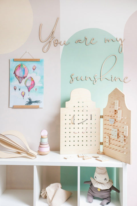 4. Child's room decor featuring 'You Are My Sunshine' wooden wall sign, pastel artwork, and wooden toys on a shelf.