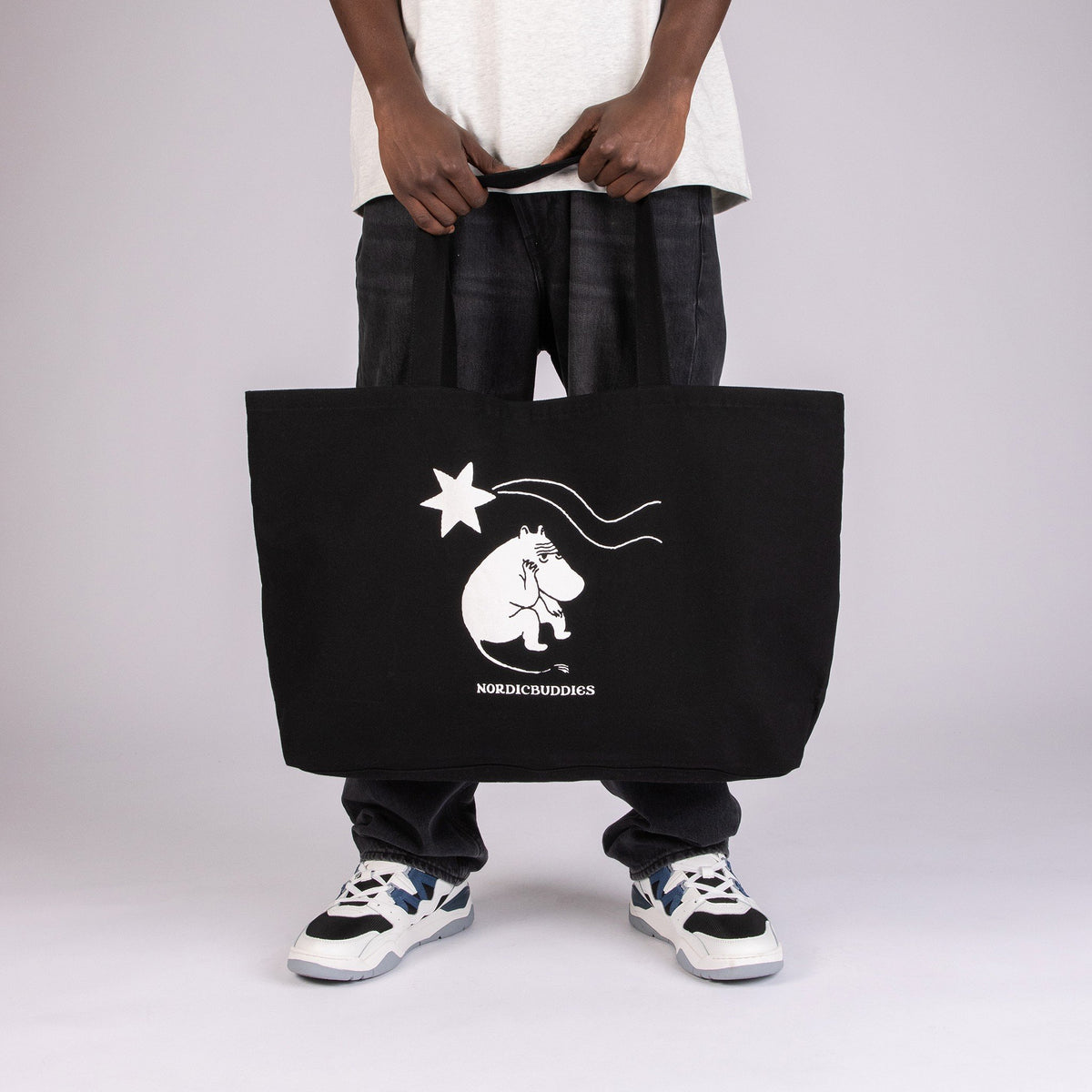 1. Unisex black XXL Novels Tote Bag by Moomin, held by a model in studio, featuring Moomin character design