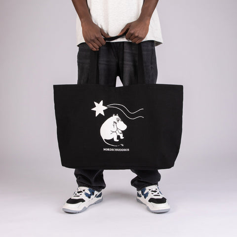 1. Unisex black XXL Novels Tote Bag by Moomin, held by a model in studio, featuring Moomin character design