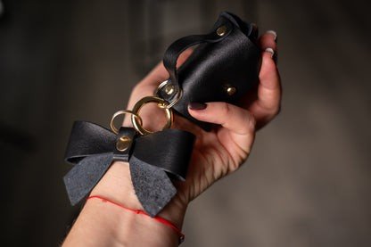 12. Close-up of Zelma Kraft mini leather charm with bow and gold hook, held in hand