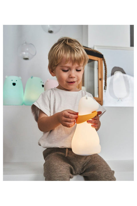 1. Child holding glowing white silicone giraffe lamp with yellow scarf in playroom